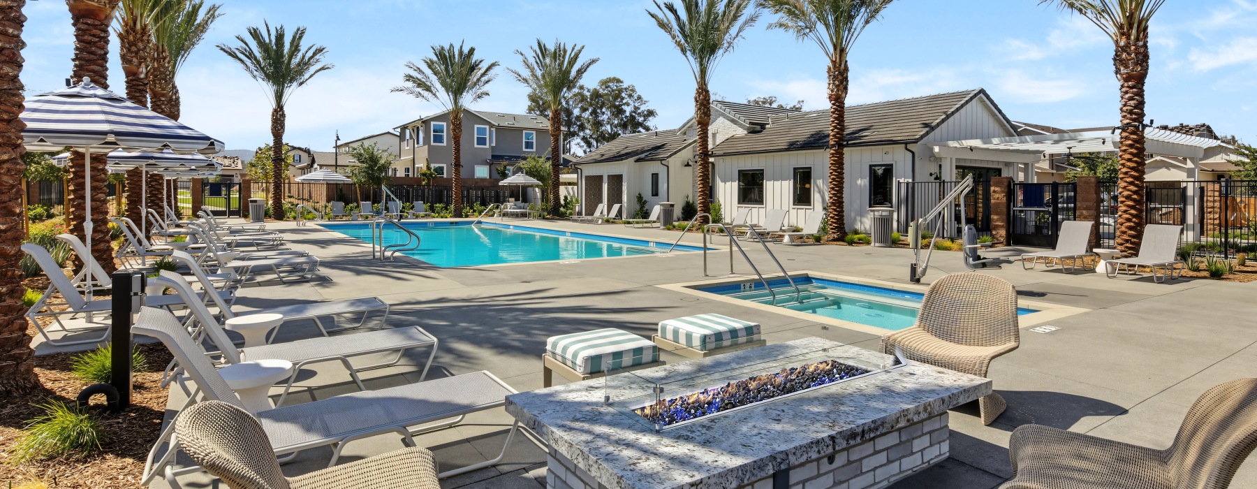 Haven’s poolside lounge area with a fire pit, lounge chairs, palm trees, and shaded seating.
