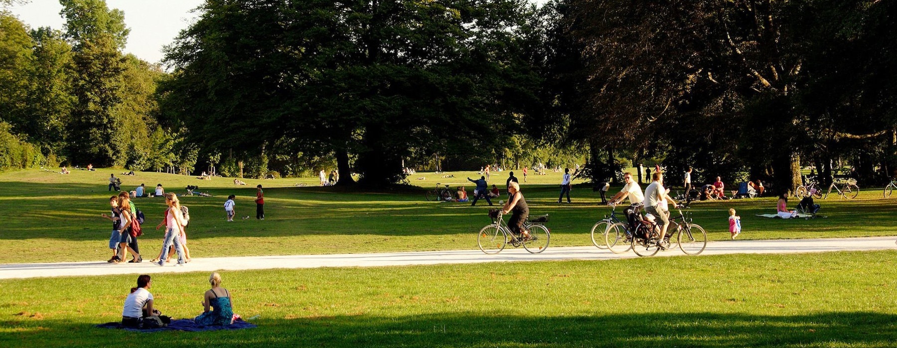A park with many people riding bikes, having a picnic, and walking.