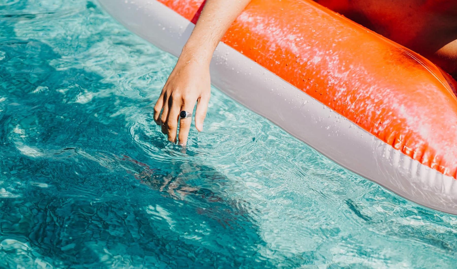 woman dangles her hand in the pool as she floats in an inflatable vessel